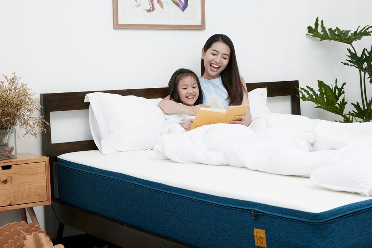người phụ nữ đang đọc sách cho em gái trên giường, hai người cười tươi