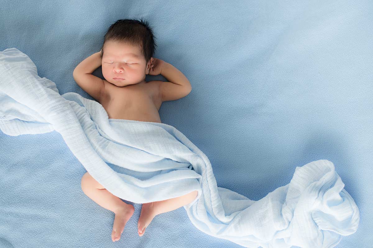 em bé vừa sinh không mặc đồ nhưng được che chắn bởi một khăn lụa màu xanh dương 